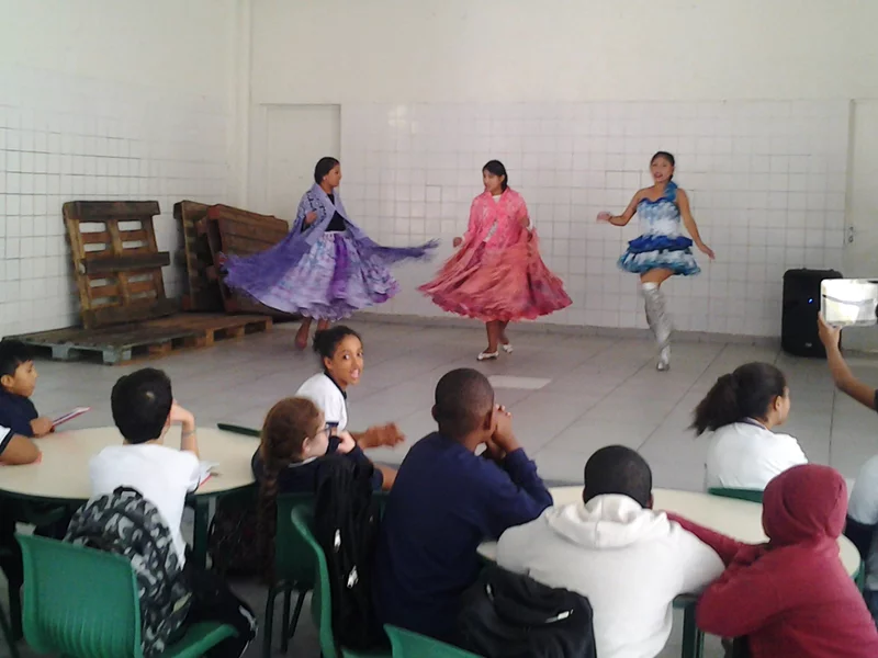 Três meninas com vestidos típicos fazem apresetação de dança boliviana em ginásio