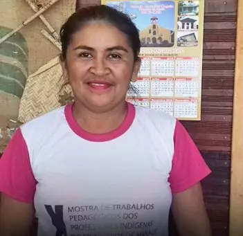 Em imagem horizontal, professora indígena Luciana Pascoal Araújo, de camiseta branca e rosa no ambiente escolar