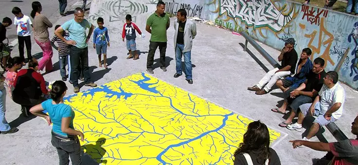 Grupo de participantes e idealizadores estão reunidos em volta de mapa que mostra os rios da cidade de São Paulo. Rios e Ruas é um dos projetos que remodelam a relação entre cidades e pessoas.