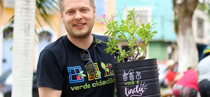 O engenheiro agrônomo Daniel Oliveira está sorrindo para a foto e segurando um vaso com uma planta. O Verde Cidadão é um dos projetos que remodelam a relação entre cidades e pessoas.