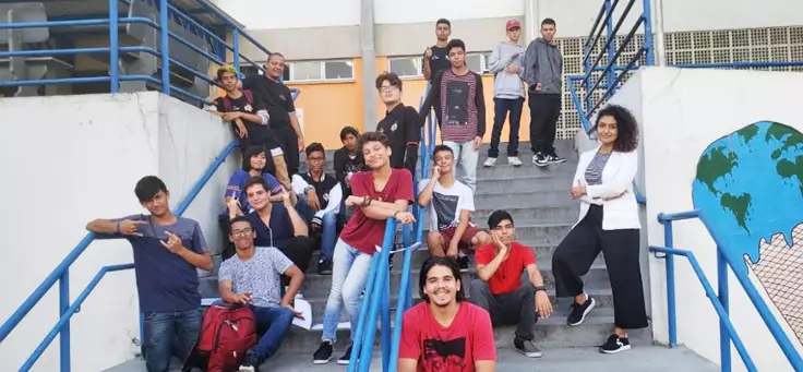 Imagem mostra grupo de alunos posando para foto, sentados em uma escada dentro da escola.