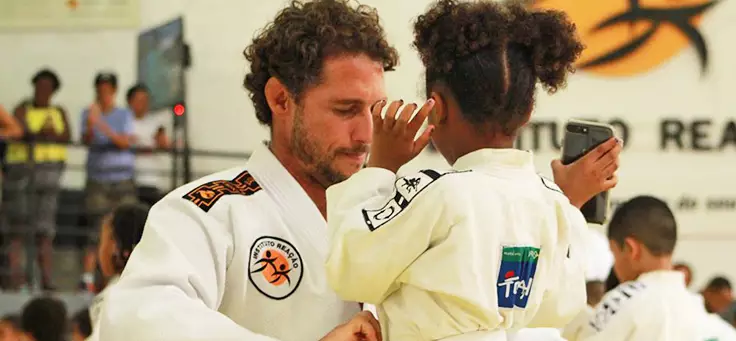 Projetos sociais esportivos: imagem mostra o ex-judoca Flávio Canto e uma criança de costas usando quimonos