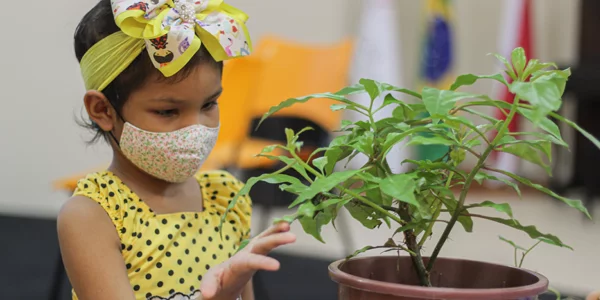 Criança usando máscara segura muda de planta em atividade na Associação Colorindo a Vida durante a Semana dos Voluntários.