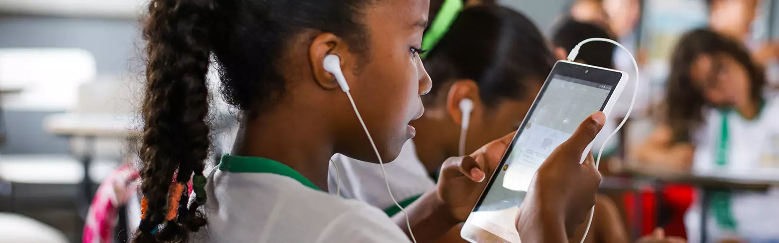 criança na escola de fone de ouvido olhando para a tela de um celular (Quem Somos)