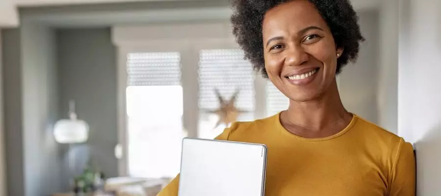 Imagem de uma mulher em uma sala de estar com livros e computador nos braços