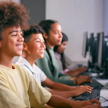 Imagem mostra quatro estudantes em perspectiva, todos estão em sala de aula utilizando computadores